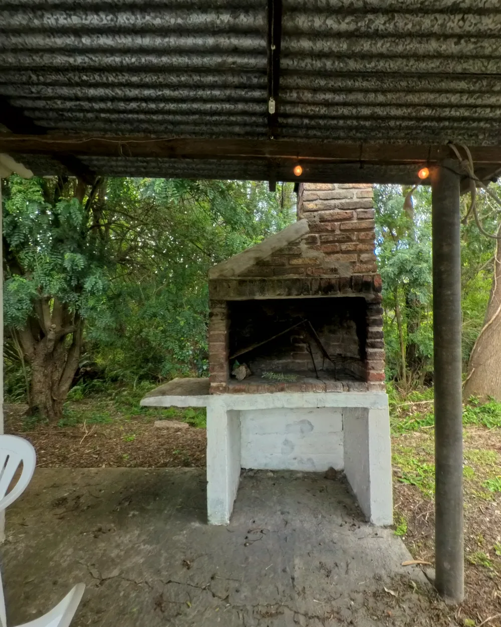Barbacoa techada con parrilla de ladrillo y el jardín atrás
