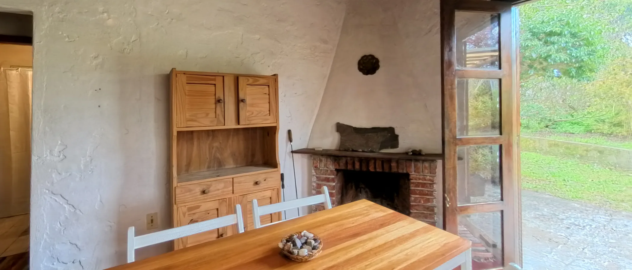 Comedor con mesa de madera y estufa a leña, con la puerta abierta al jardín